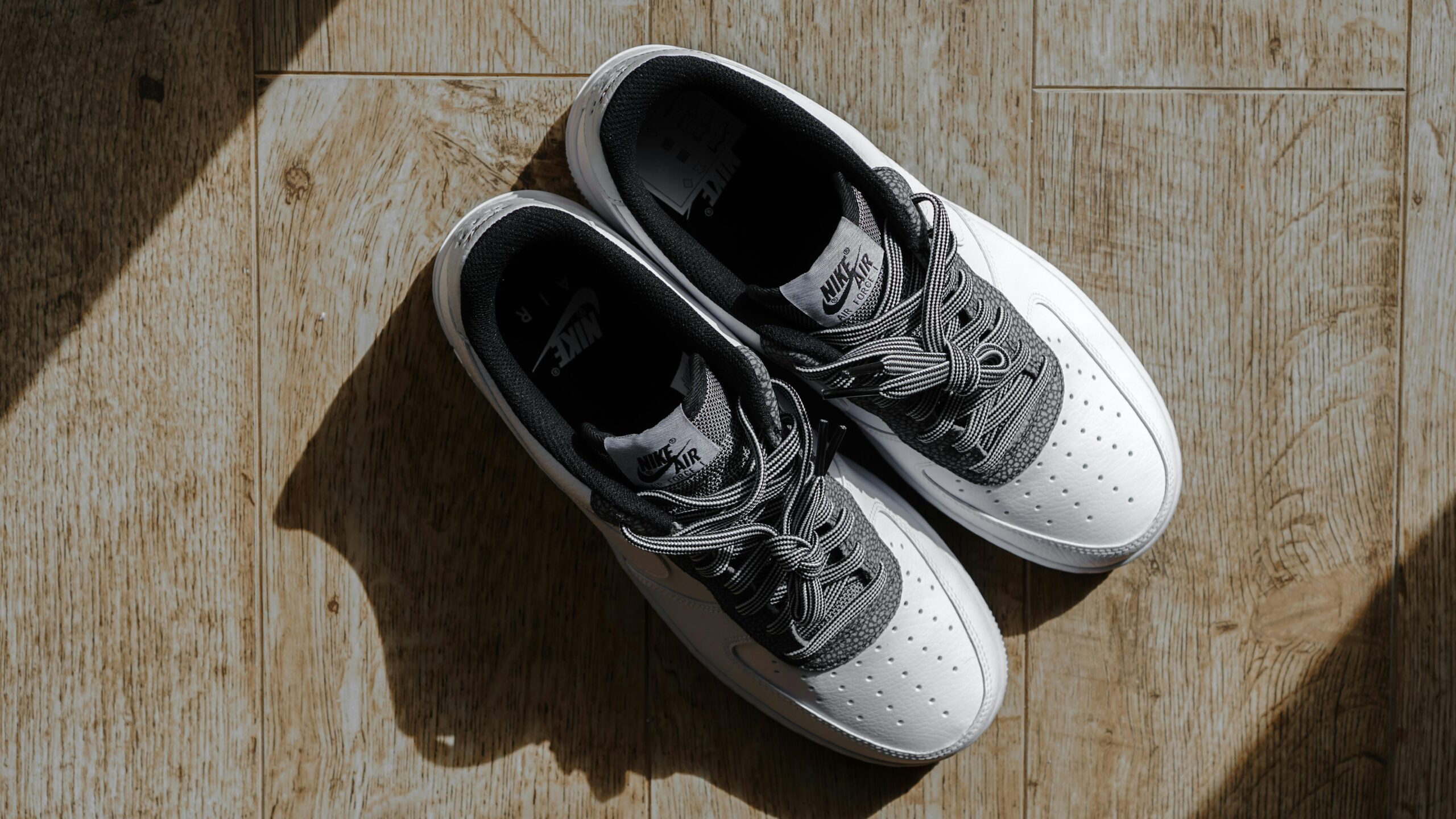 White sneakers displayed on a wooden floor with natural lighting, showcasing fashion footwear.