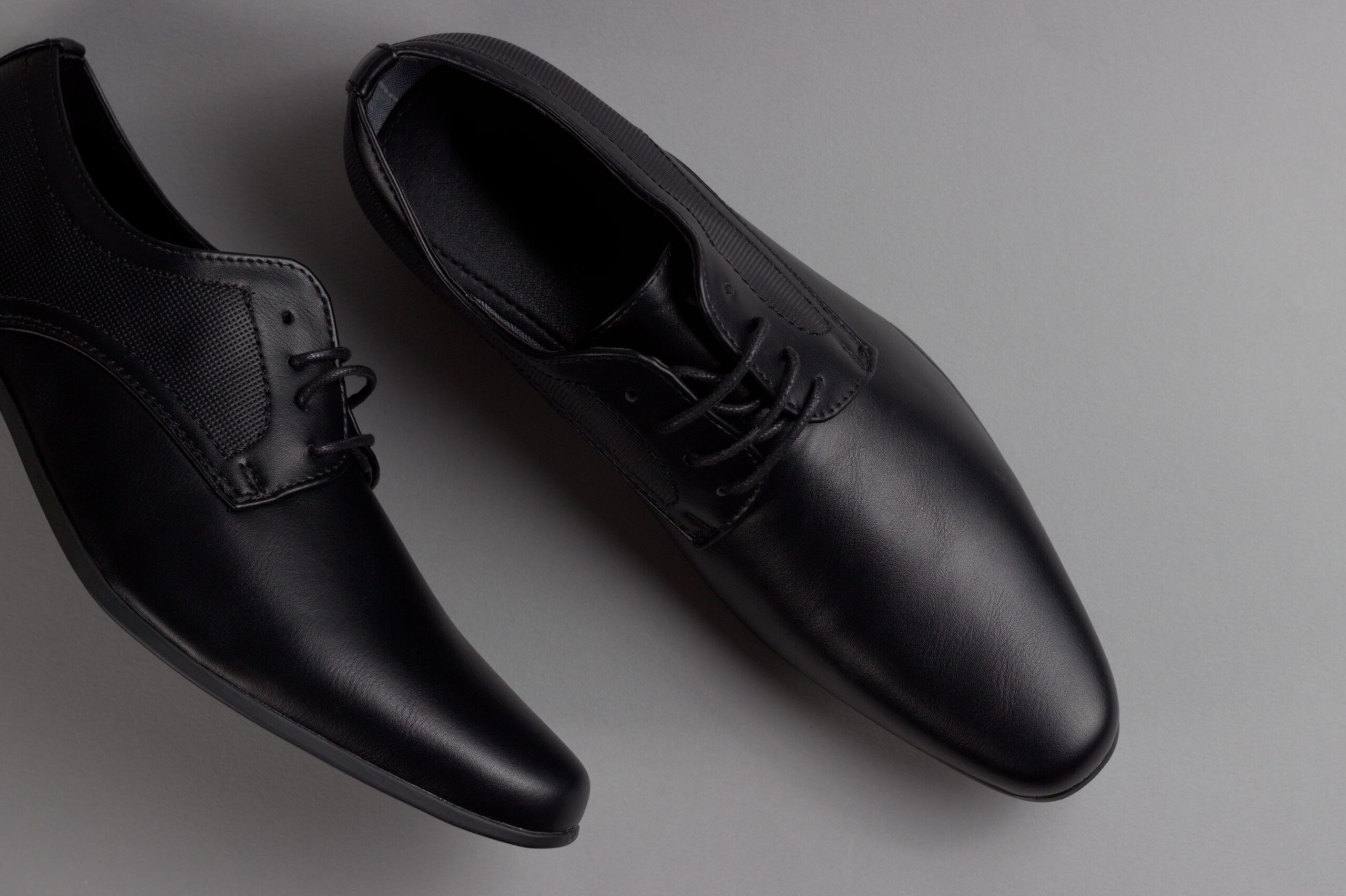 Pair of stylish black formal shoes displayed on a minimalist grey background, perfect for business attire.