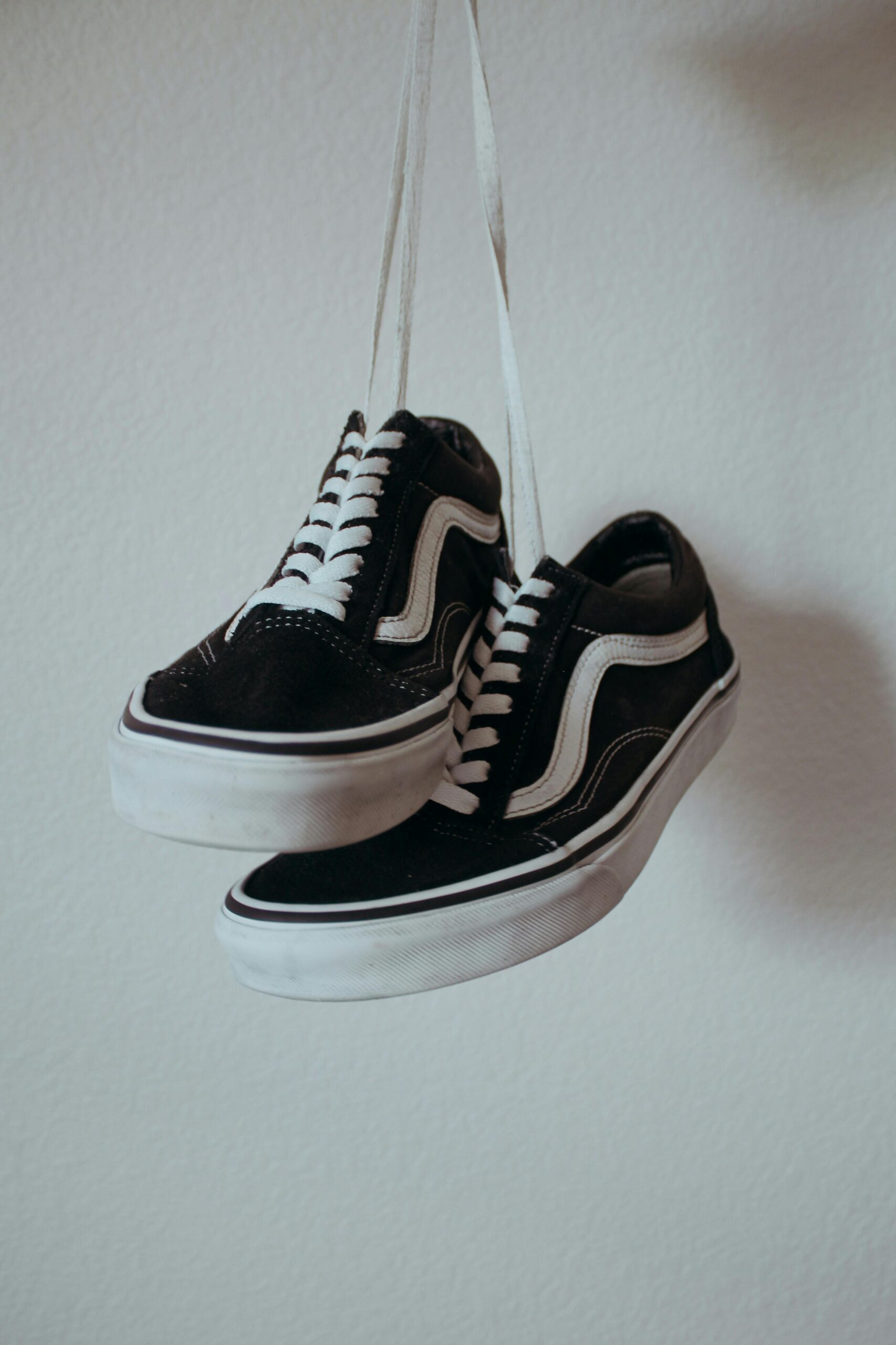 Black sneakers with white shoelaces hanging on a wall.
