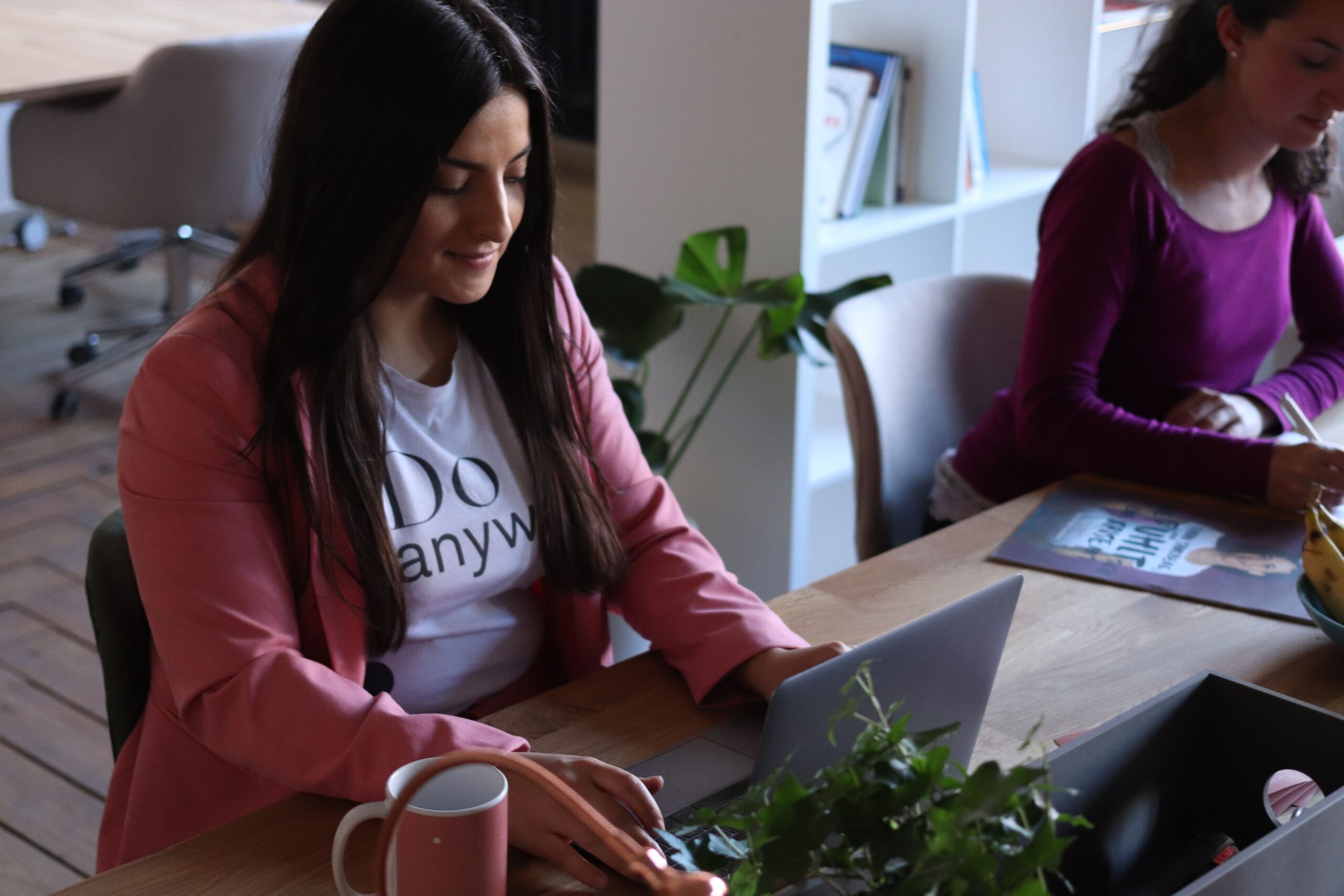 Two women working at laptops in a stylish office space, focused and productive.